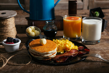 Pancake stack, eggs, bacon, syrup, milk, cup of fruit