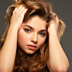 Closeup portrait of an young adult girl with long curly hair.  Photo of a fashion model posing at studio. Pretty young woman with long brown hair looking at camera. Beauty portrait.