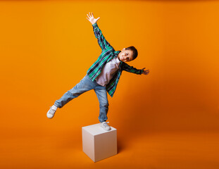 happy little boy smiling and holding balance, standing on one leg on a cube in the studio.