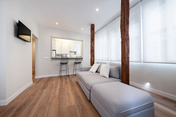 sofa with chaise longue with old wooden pillars and in the background a window to the kitchen in a vacation rental apartment