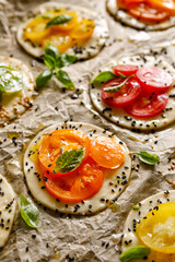 Raw mini tarts mde of puff pastry and tomatoes of different colors and varieties sprinkled with herbs prepared for baking, close up view 
