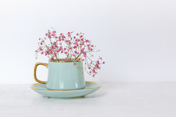 Turquoise cup with beautiful pink gypsophila flowers on a light background, minimalism, copying...