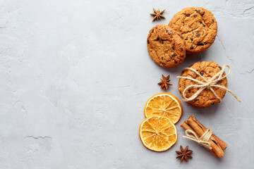 Top view of oatmeal cookies with chocolate chips tied with string, anise, dried orange slices and cinnamon on a gray stone background. Christmas pastries. Copy space.