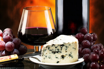 Taça e garrafa de vinho tinto. Uma fatia de queijo gorgonzola. Um cacho de uva Thompsom mais um...