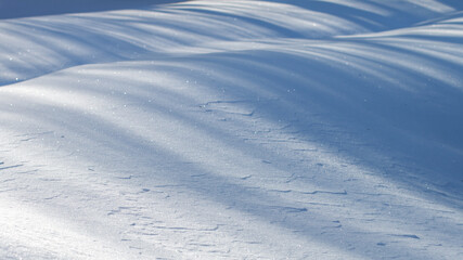 beautiful sparkling snowy landscape with hills of snow, strips of shadows and bright beams of sun. space for text, seasonal winter scenery background with trick of light 