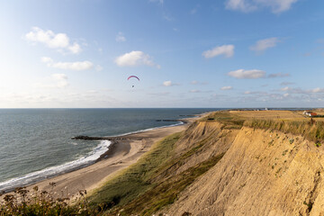 Fototapeta na wymiar Paraglider soaring along the cliffs of Bovbjerg, Denmark during sunset. Scenic view from top of the cliffs onto the sea 
