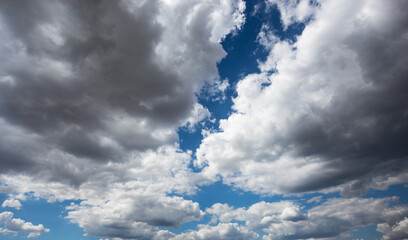 Blue cloudy sky with darker clouds. The clouds are bright on the periphery with a darkening color...