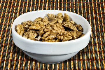 Walnuts in a white bowl on a brown wooden mat.