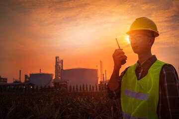 A construction engineer, a young engineer holding a radio and wearing a helmet standing in front of the refinery, exploring new plans and expanding the factory, Silhouette engineer standing.