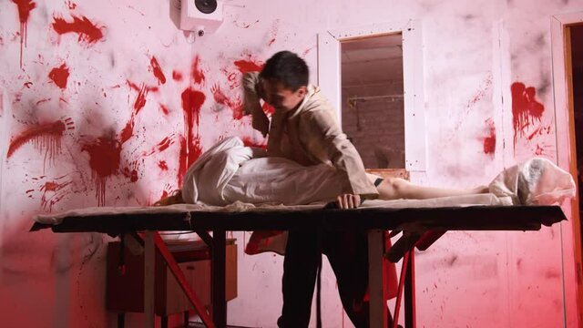 Horror acting - the doctor ties the mad girl to the table in the bloody room of mental hospital