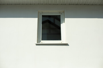White window in a white wall. A small window made of plastic in bright sunlight. Exterior of the building.
