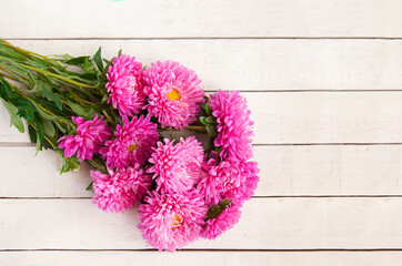 A beautiful bouquet of pink asters lies on a white wooden background, copy space