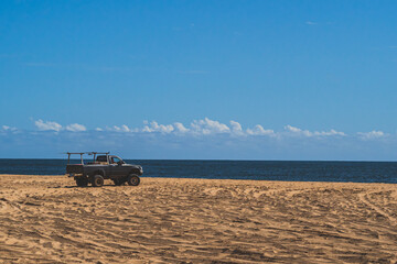 Off road vehicle on sandy beach against blue sky and ocean