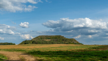Fototapeta premium Closed city dump. Restoration of the territory. Landscaping of a large hill of garbage. In the background is a metropolis and a blue sky with clouds. Ecological problem.