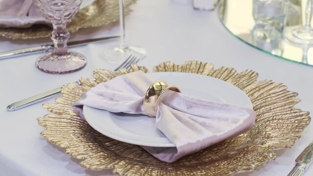 Banquet, restaurant. Table setting. Plates, cutlery, glasses. There is a white tablecloth on the table. Peach napkin with gold ring. Compositions in peach-pink tones 