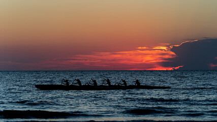 Rowing crew in silhouette on water against pastel sunset sky © RandomHartz