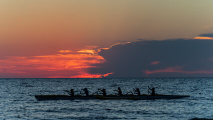 Rowing crew in silhouette on water against pastel sunset sky