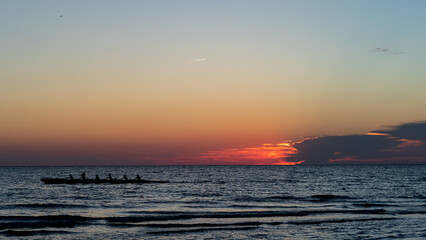 Rowing crew in silhouette on water against pastel sunset sky