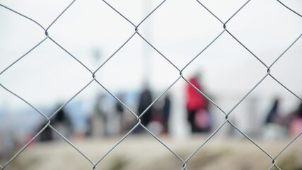 Barbed wire in refugee camp. Migrants behind chain link fence in camp. Group of people behind fence. Concept of prison, freedom, barrier, security and migration. Refugees on their way to EU.	