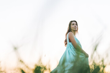 Close up portrait of Young beautiful carefree long hair woman in light blue turquois dress in sunset field. Sensitivity to nature concept, feminity