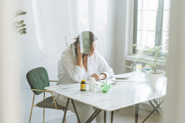 Thinking brunette woman doctor nutritionist plus size in white shirt working on table with house plant in bright modern office room