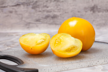 Ripe yellow tomatoes on cutting board with gray background.