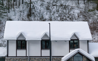 Attic with three windows in a mountain house. Background - a mountainside with trees. White snow covers roof of mansard. Chalet concept in winter season.