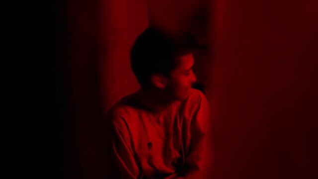 Mad man in straitjacket trying to get out of the clothes in the cell of mental hospital in red lighting