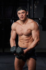 Fototapeta na wymiar a muscular young man with a naked torso holds two black dumbbells in his hands in a gym