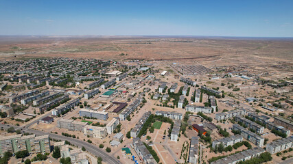 Fototapeta na wymiar Drone view of the small town of Balkhash. The city is located on the shore of a lake. Low houses, free streets and roads. Green trees grow and there are sports grounds. There is a steppe around city