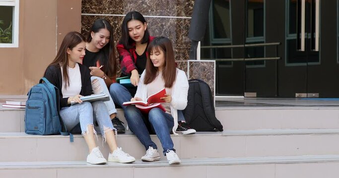Group of 4 college close friends sitting together on school building downstairs taking and discussing education and studying with intimate manners. Concept of teenager students lifestyle.