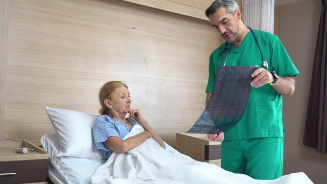 doctor using brain X-ray film explain the symptoms to the senior patient after treatment . surgeon Talking With old woman patient on bed in the hospital .