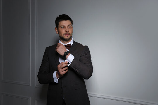 Man wearing stylish suit and cufflinks near white wall