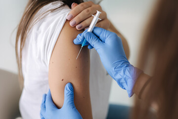 Close-up of female doctor in protective gloves holding syringe making covid 19 vaccination. Women getting injection in shoulder. Vaccine clinical trials concept, corona virus