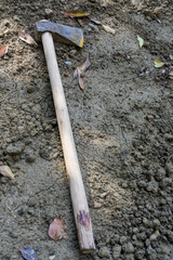 An isolated shot of a metal axe with wooden handle lying in the soil.