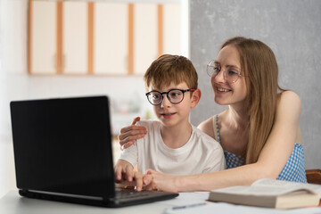 Mother and son are doing homework on the computer. Sister helps her brother with lessons. Tutor explains topic to child.