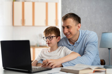 Dad helps his son do homework. Boy is doing homework with his father. Dad teaches his son to work with computer program.