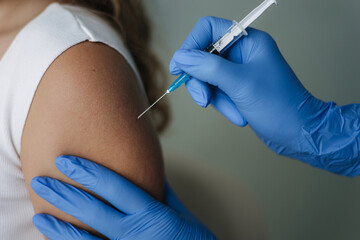 Female doctor in protective gloves holding syringe making covid 19 vaccination. Women getting injection in shoulder. Vaccine clinical trials concept, corona virus