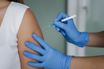 Female doctor in protective gloves holding syringe making covid 19 vaccination. Women getting injection in shoulder. Vaccine clinical trials concept, corona virus