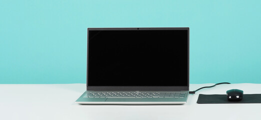 Computer laptop or notebook with mouse and pad on white desk and mint green background.Studio shot.