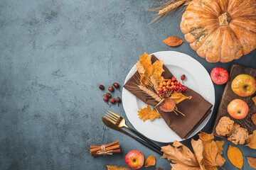 A plate, cutlery, autumn leaves, apples and a pumpkin on a dark gray-blue background. Top view,...