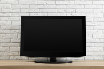 Modern TV set near white brick wall indoors