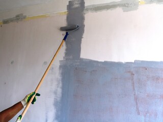 a painter's roller on a long handle in a gloved hand, painting the wall of the room in gray, painting the walls of the apartment with your own hands