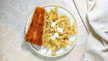 Boiled gluten-free pasta with a fish cutlet in a plate.