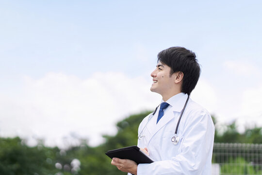 青空背景で笑顔で立つ男性医師