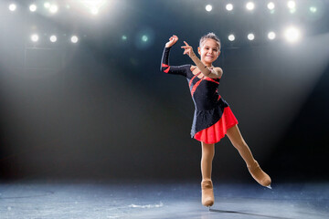 Fototapeta na wymiar Little skater rides on rings in red and black dress on ice arena