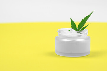 Natural hemp cosmetics. An open jar of body cream and hemp leaves on a yellow background.
