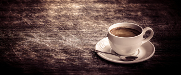 A white cup of coffee  and silver coffee spoon on a dark wooden table