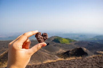 Young woman holding a volcano stone with a heart shape of the Crater Silvestri in Mount Etna in Catania.  Holidays background.