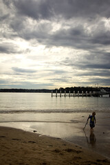 Small boy silhouette in forground of water with ferry jetty background. Textured cloudy sky. One person. Space for copy 